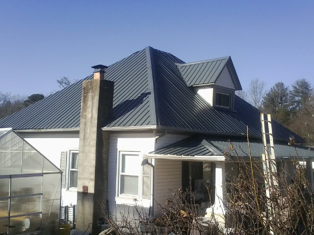 Dark blue standing seam metal roof on a white farmhouse with dormer — Slate & Tile Roof Repair by Roofing Brothers in Kitty Hawk
