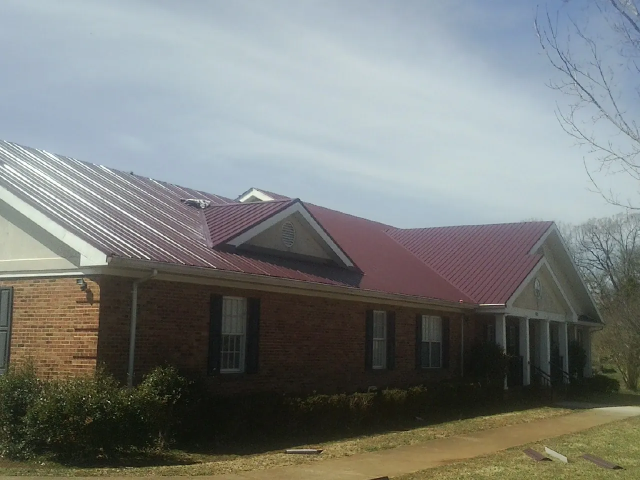 Red metal roof with gabled entries on a long brick building, from a Hail Damage Roof Repair job in Kitty Hawk