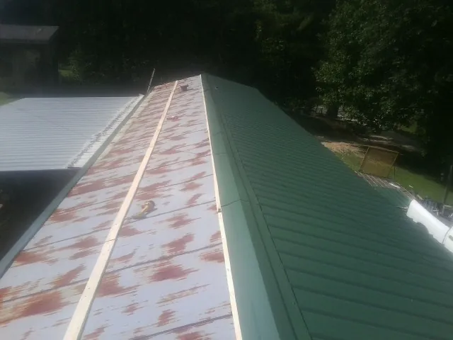 Old rusted panels beside newly installed green metal roofing — Wind Damage Roof Repair by Roofing Brothers in Kitty Hawk