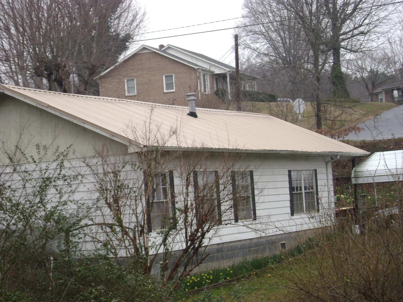 Tan metal roof on a white sided house set into a hillside — Commercial Roofing by Roofing Brothers in Kitty Hawk