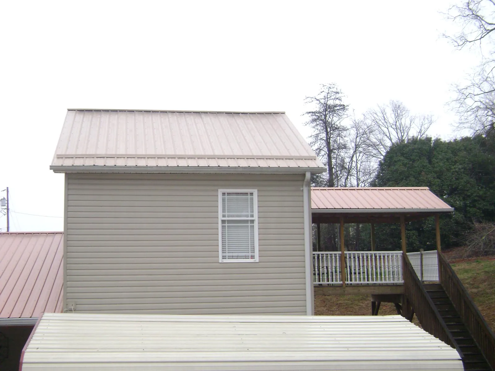 Tan metal roofs on a two story addition and attached porch, from a Roof Replacement job in Kitty Hawk