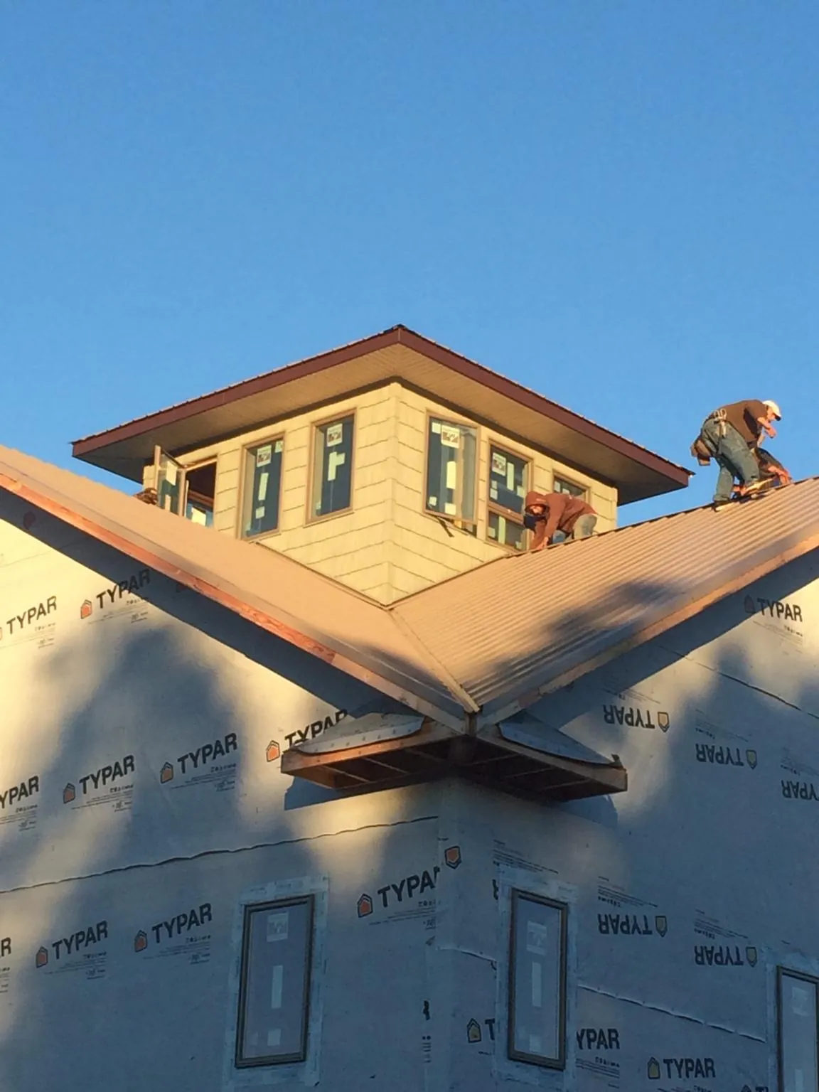 Roofers working around a rooftop cupola on a new metal roof at sunset — Roof Waterproofing in Kitty Hawk by Roofing Brothers